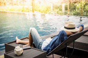 Happy man with a hat who is relaxing on a sunbad next to a pool filled with sustainably desalinated water. The man has no bad conscience anymore as the water is purified in a sustainable way.