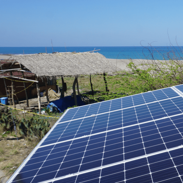 Solar panels that are providing the necessary power to run the desalination system. The generated energy is partly stored in a battery (with a long life-span), which ensures water supply in periodes with shortages in sunlight. In the background there is a small fishing hut and a beach.