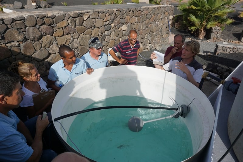 Several people standing around a circular water tank and an employee explaining the desalination process