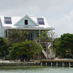 Villa in Belize with a small pier leading into the water and solar panels on the roof, which are providing green energy for the desalination process.