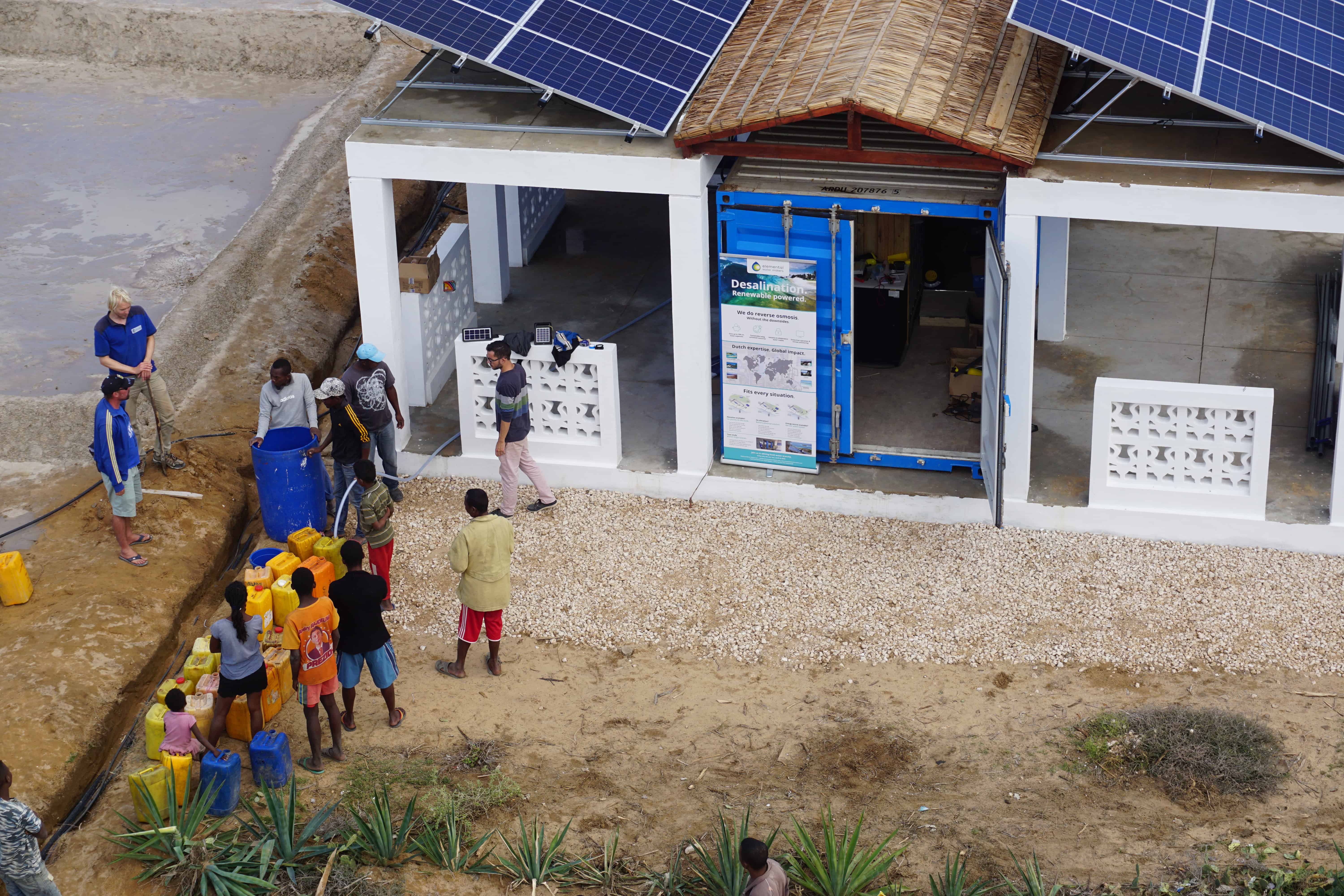 Villagers waiting for the desalination unit to be activated, building a queue in front of the container with their water tanks