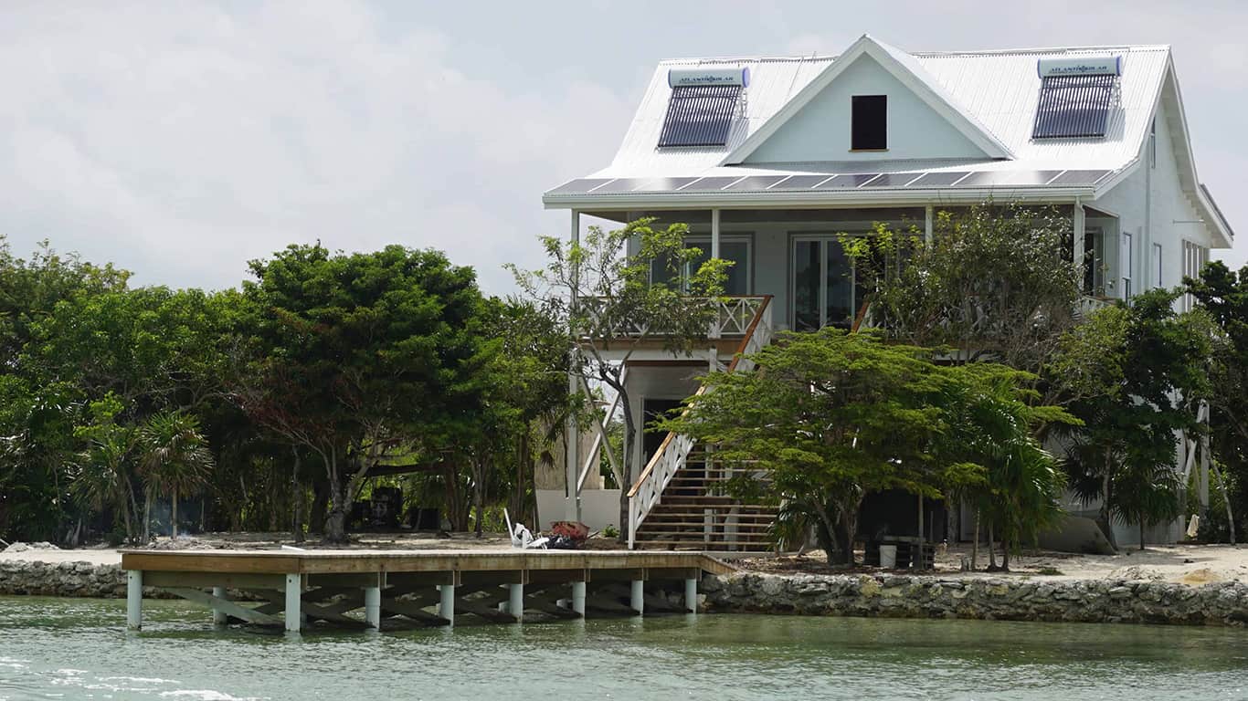 Villa in Belize with a small pier leading into the water and solar panels on the roof, which are providing green energy for the reverse osmosis desalination process.
