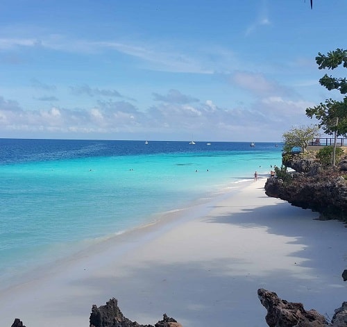 White beach with rocky cliffs in Tanzania, next to the off grid solar purification machine that was manufactured by elemental water makers to provide clean desalinated water.